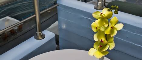Una bandeja con una taza de café, una tetera y un florero con flores en un balcón con vista al mar.