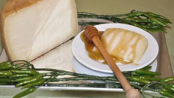A large wheel of cheese, a bowl of honey, and green chili peppers on a tray.