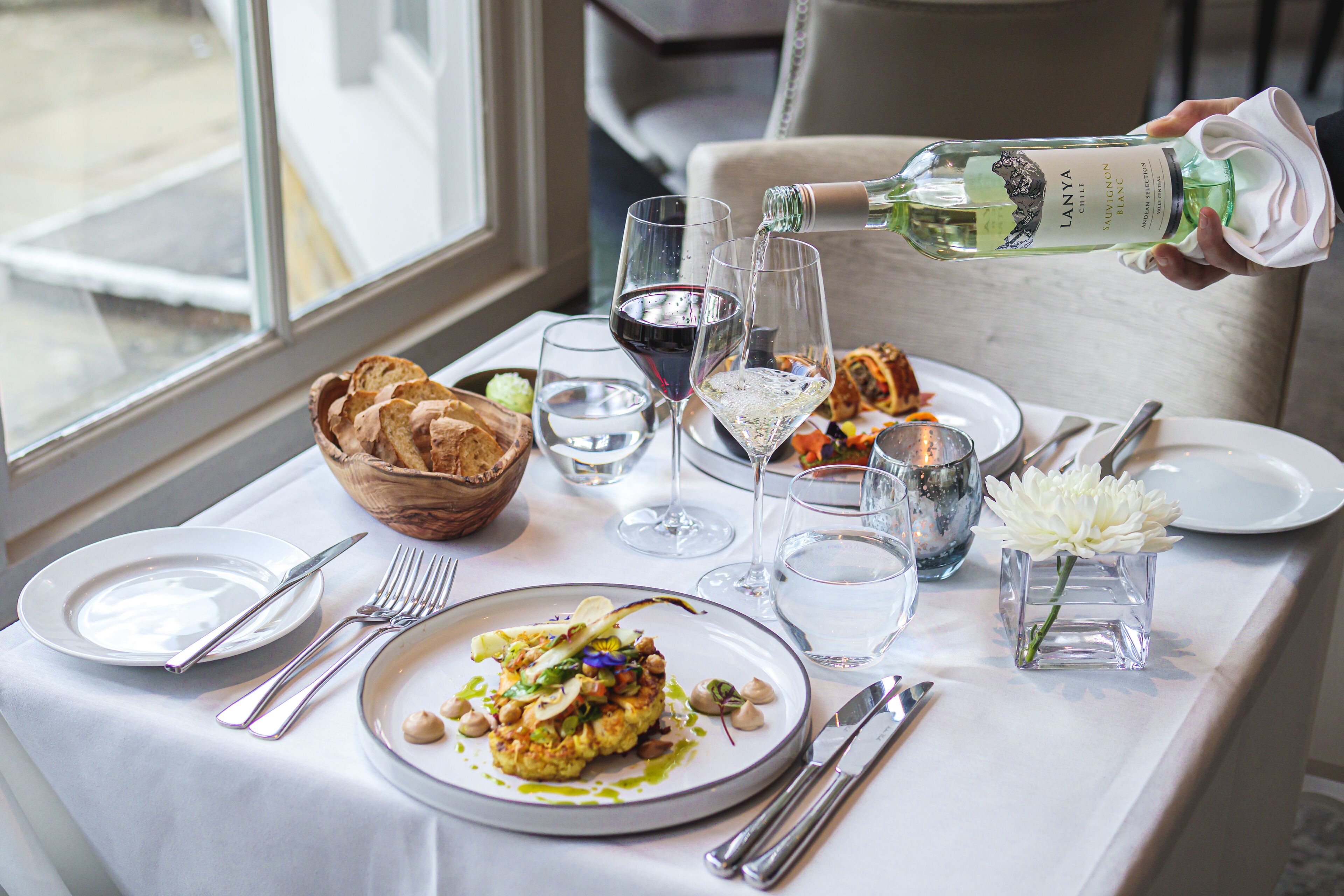 Una mesa de comedor dispuesta con platos, cubiertos, vasos y una botella de vino blanco frío Lanya.