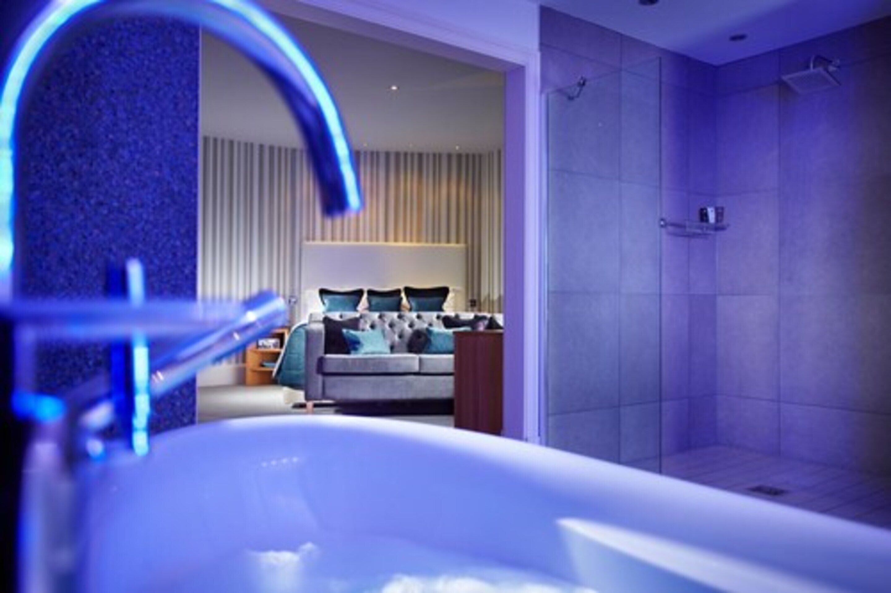 Une salle de bain moderne avec une baignoire, une douche et un espace chambre ouvert, comprenant un lit et des rideaux.