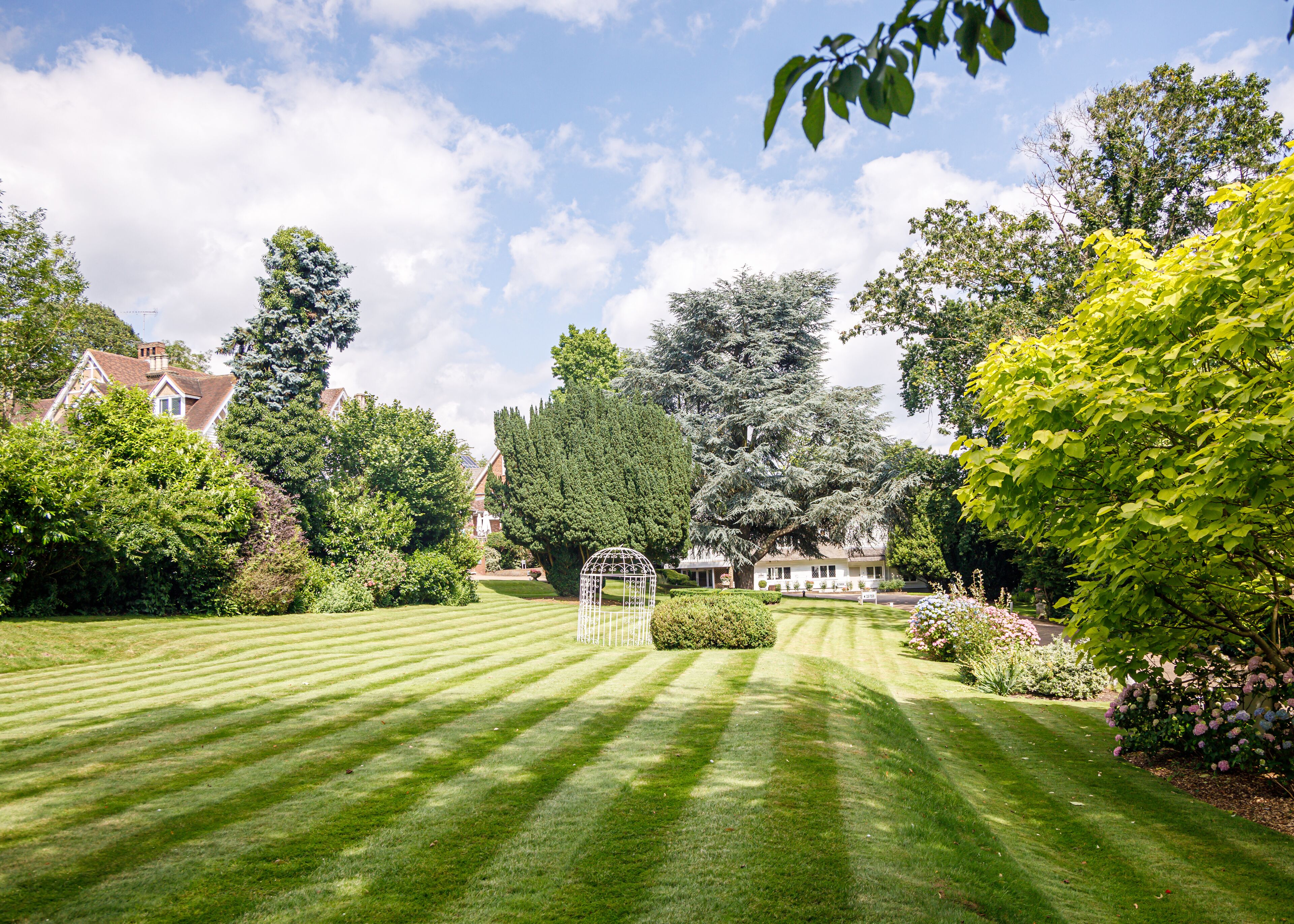 A well-manicured lawn with a gazebo, surrounded by mature trees and a house in the background.
