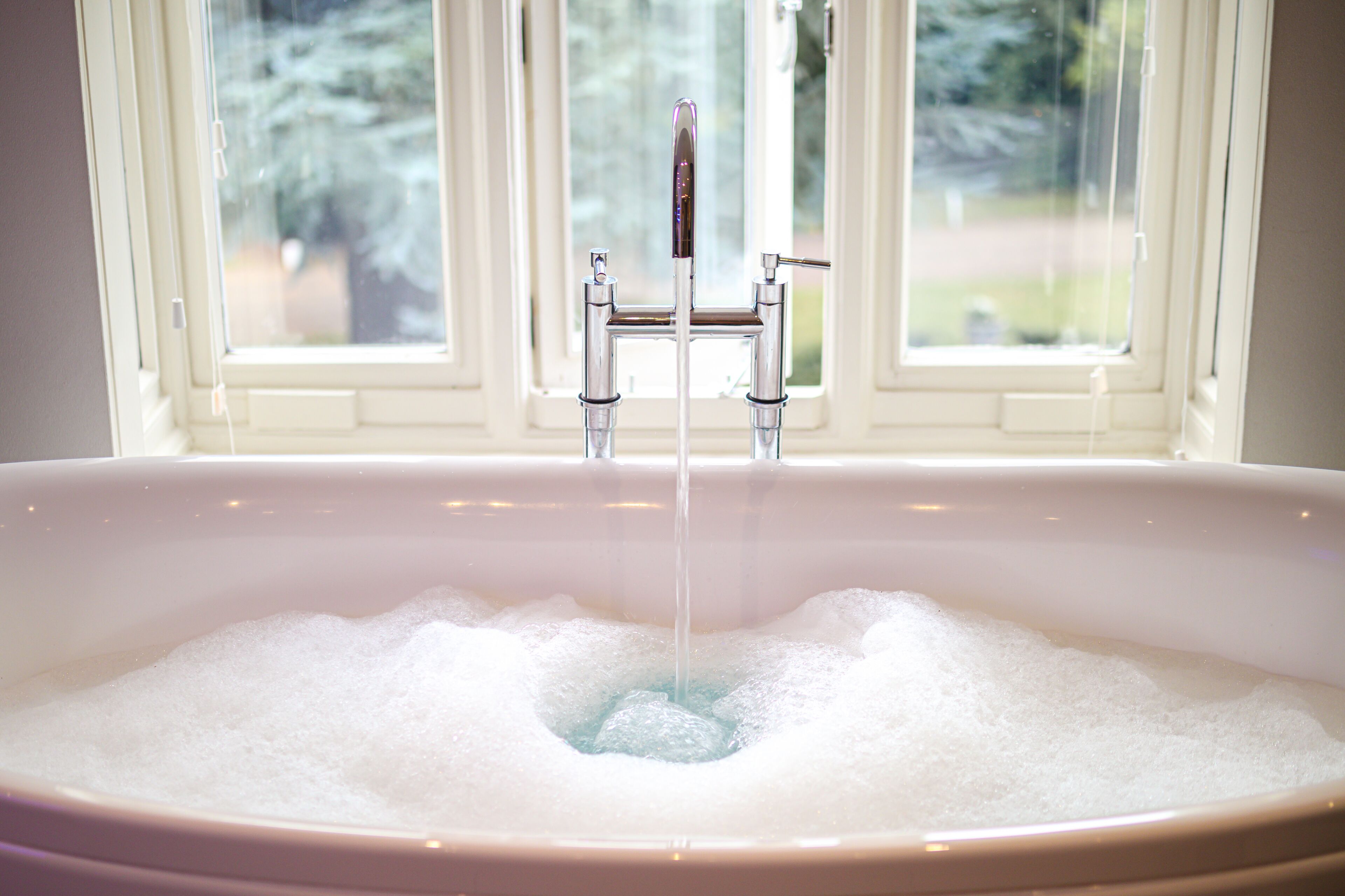 A bathtub filled with bubbles, a faucet, and a window in the background.