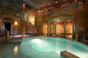 Una piscina interior con suelo de baldosas, una escalera con barandilla y una pared con un mural.