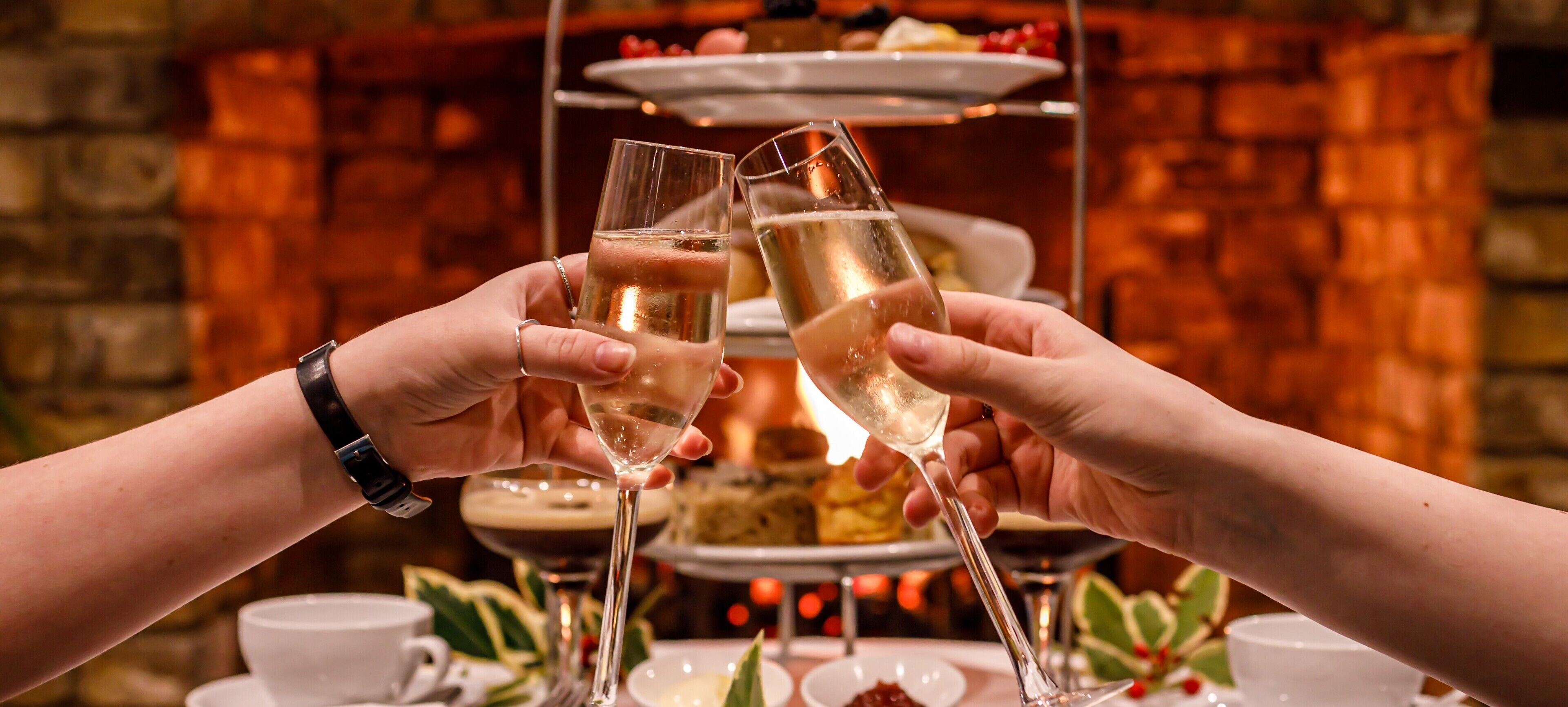Due mani che brindano con flute di champagne. Sullo sfondo, un vassoio a più piani con piatti per dolci.