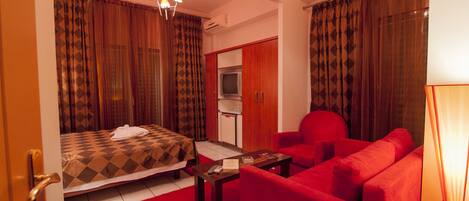 A hotel room with a bed, a red sofa, a small table, a TV, and curtains.
