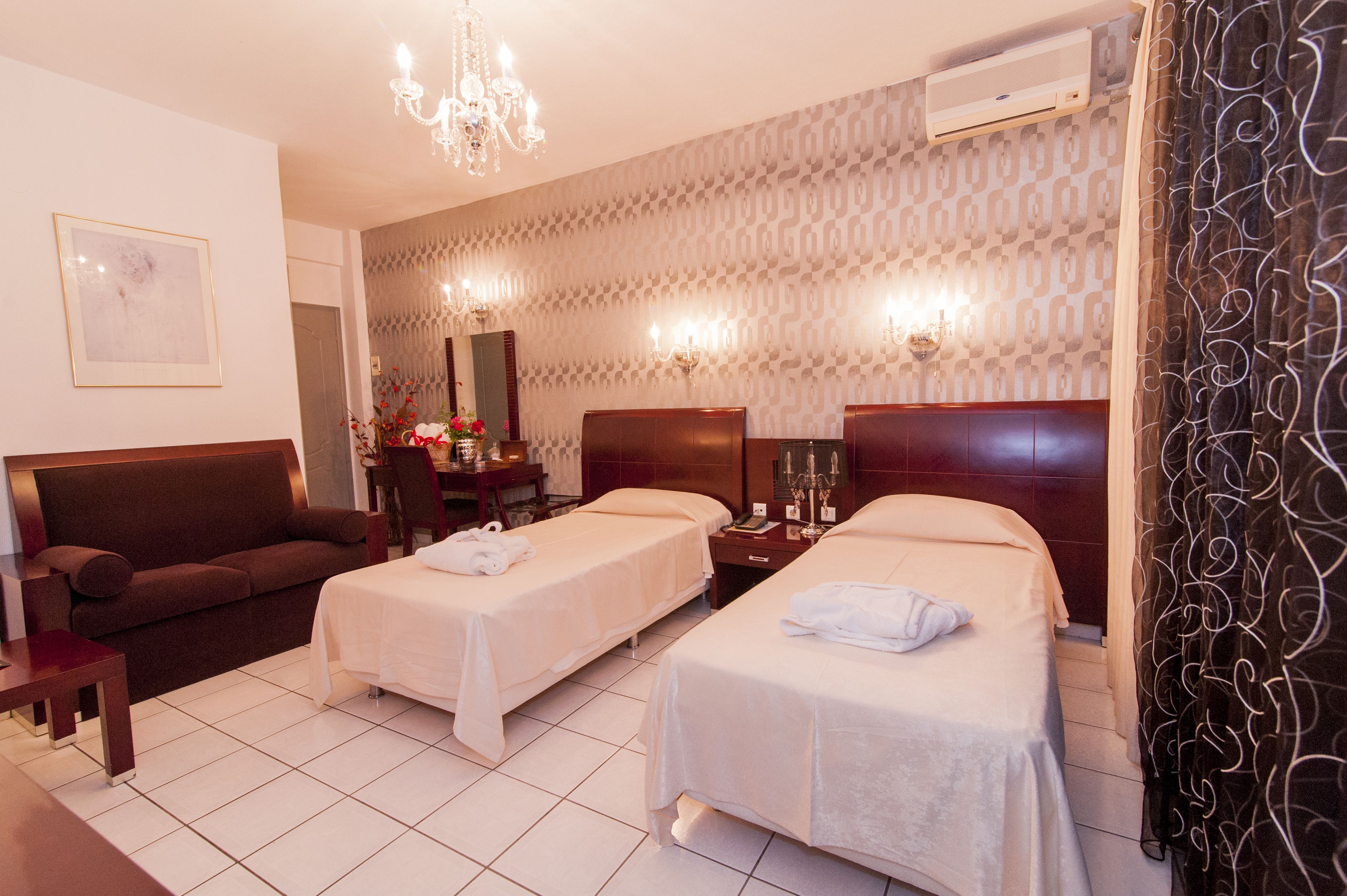 A hotel room with two single beds, a sofa, a desk, and a chandelier.