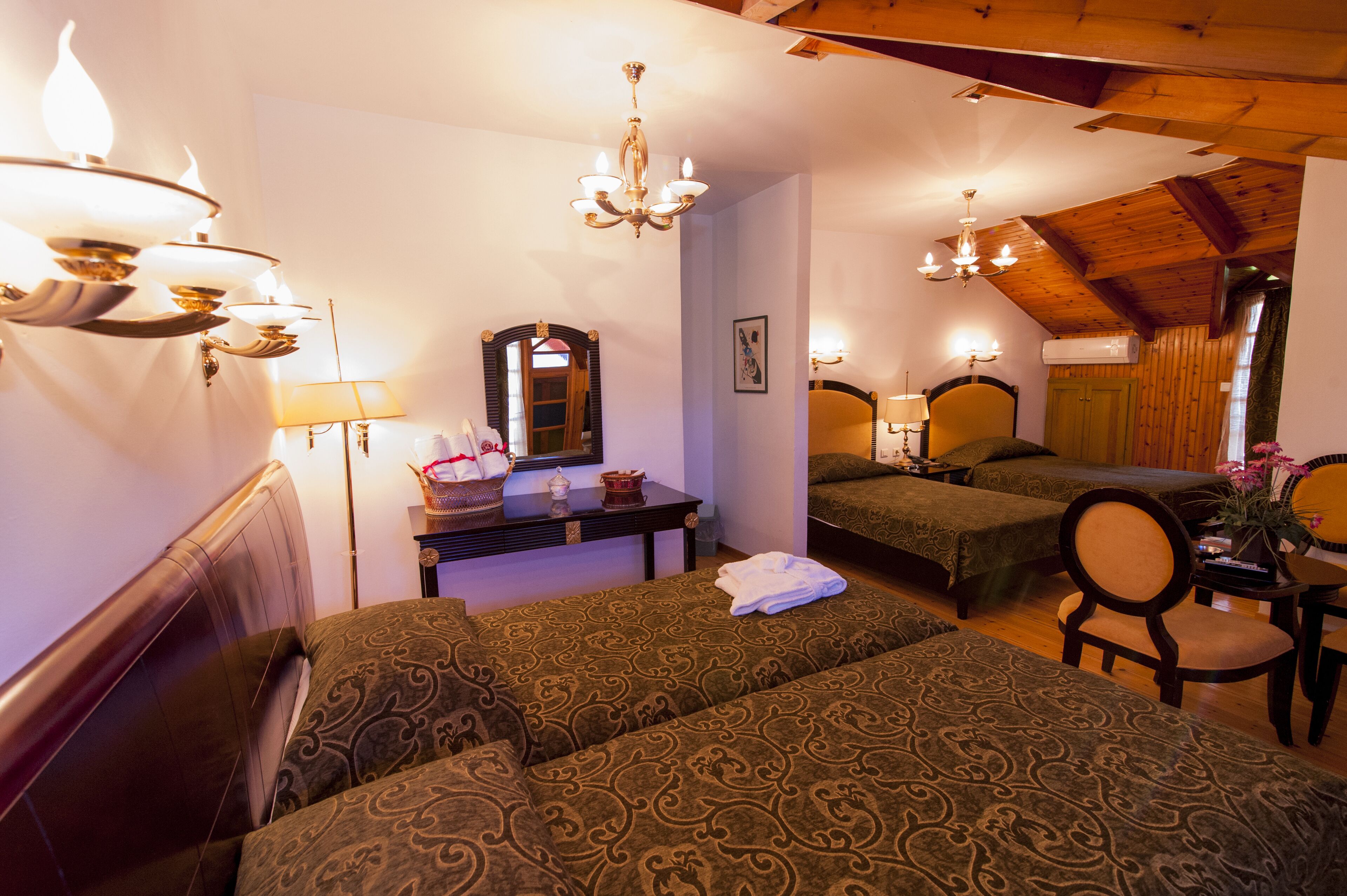 A hotel room with two beds, a sitting area with a chair, a small table, a mirror, and a chandelier.
