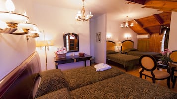 A hotel room with two beds, a sitting area with a chair, a small table, a mirror, and a chandelier.