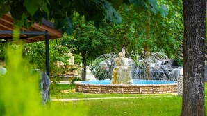 A fountain with water jets in a circular stone basin, surrounded by grass and trees. - Krikonis Hotel (Ioannina)