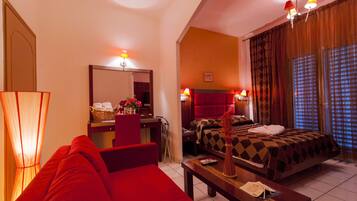 Ein Hotelzimmer mit rotem Sofa, einem Bett mit kariertem Überwurf, einem Schreibtisch mit Lampe und einem großen Fenster mit Vorhängen.