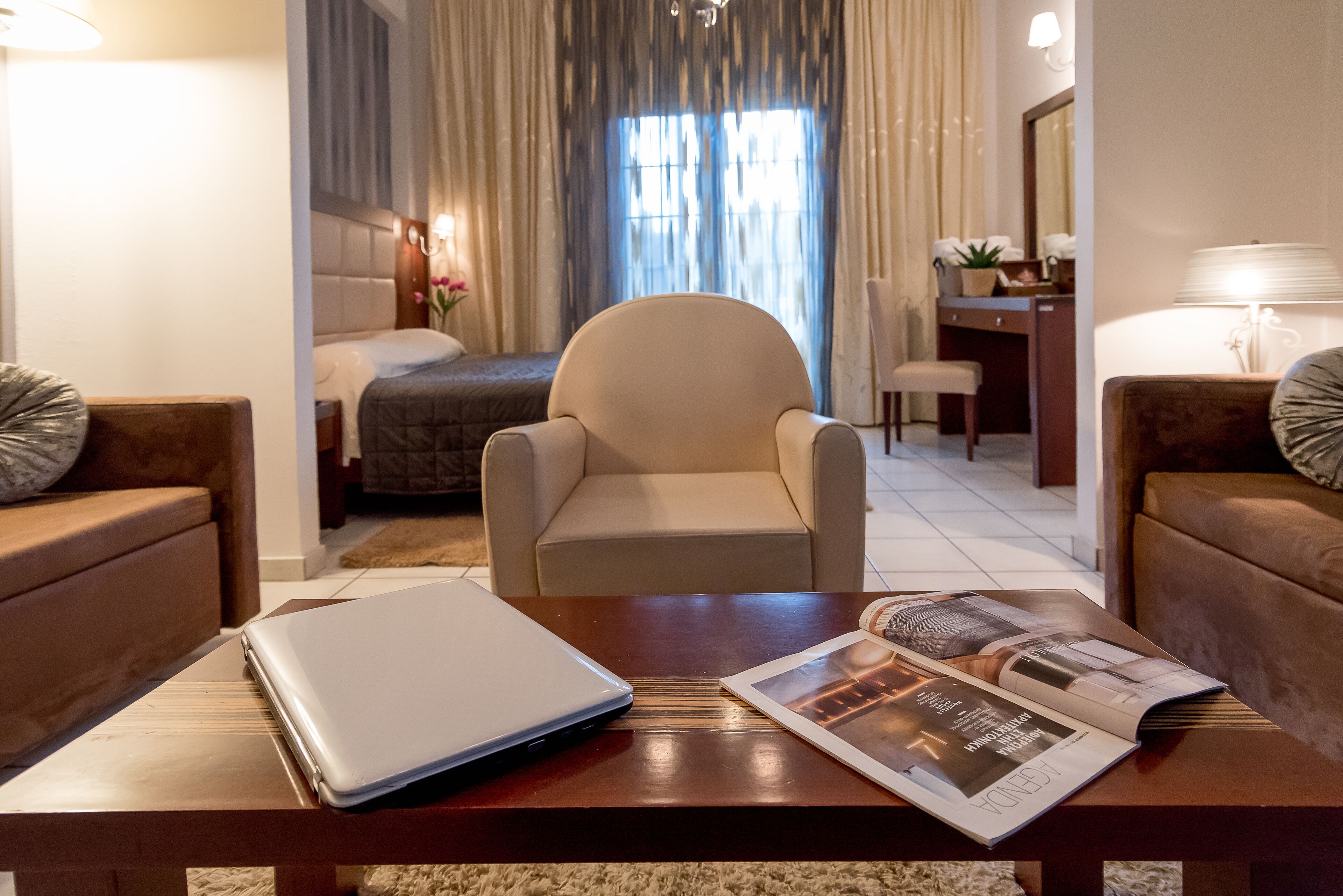 Una habitación de hotel con una cama, una silla, un escritorio, una laptop y una revista sobre una mesa.