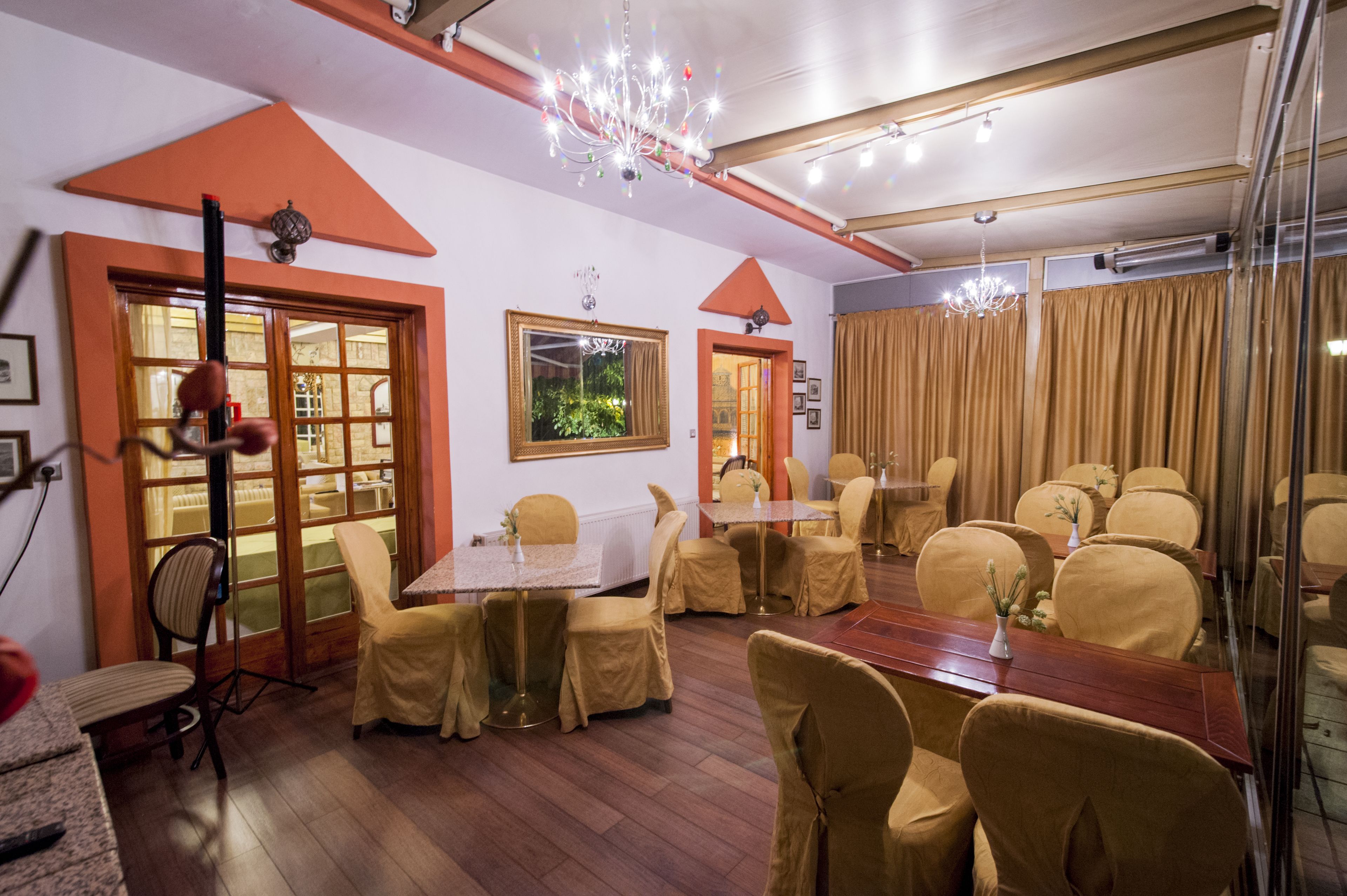 Un comedor con una larga mesa de madera, varias sillas y una lámpara de araña. Hay ventanas amplias con cortinas, una puerta que da a otra habitación, y un techo con vigas a la vista y luminarias.