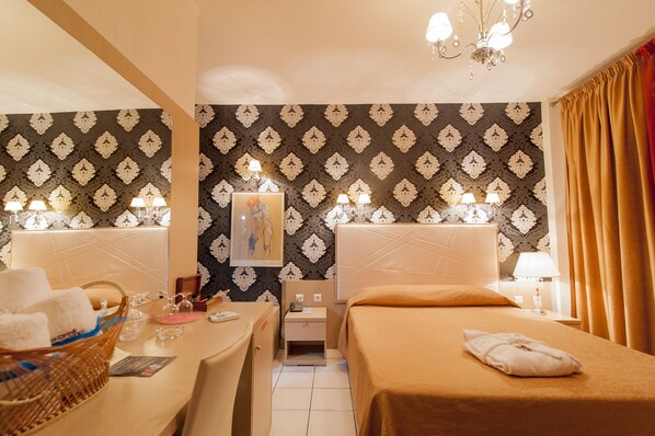 Classic design with a large bed and seating area, featuring a repeating pattern wallpaper and a chandelier.