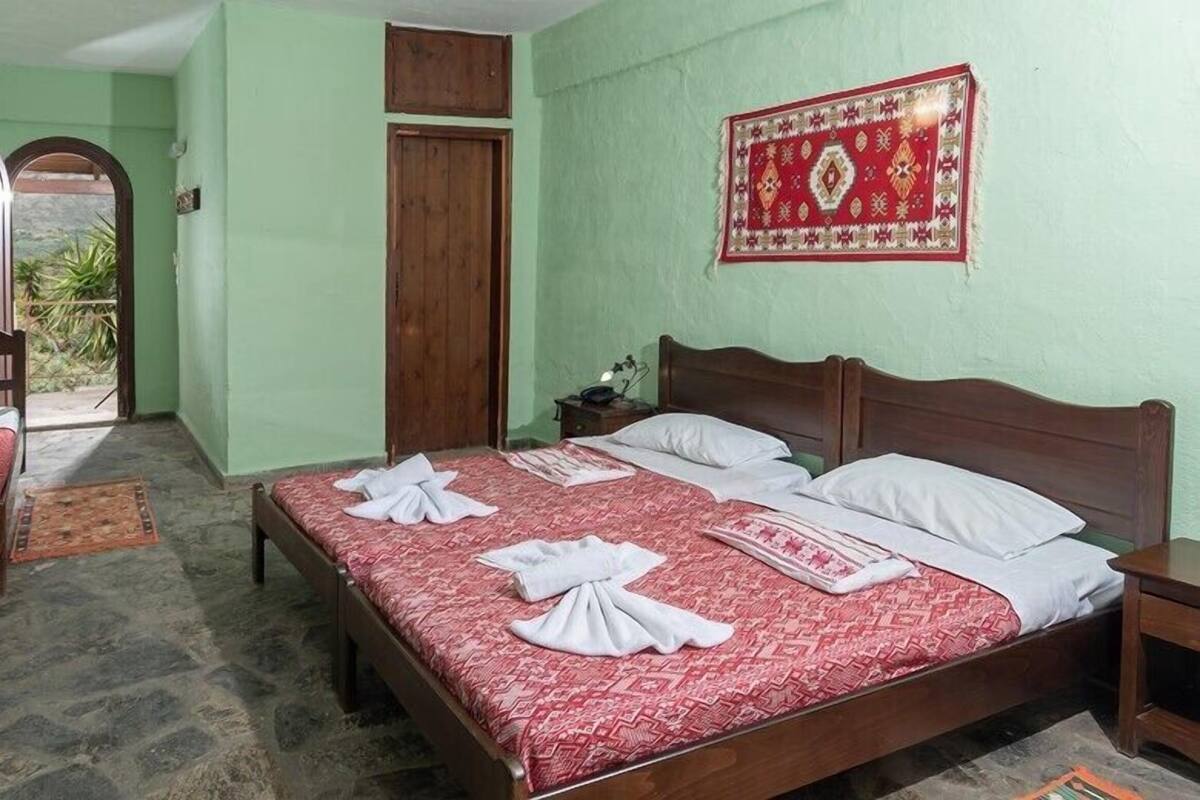 Ein Zimmer mit einem Bett, einem Schreibtisch und einem Stuhl. Eine Tür und ein Fenster sind vorhanden.