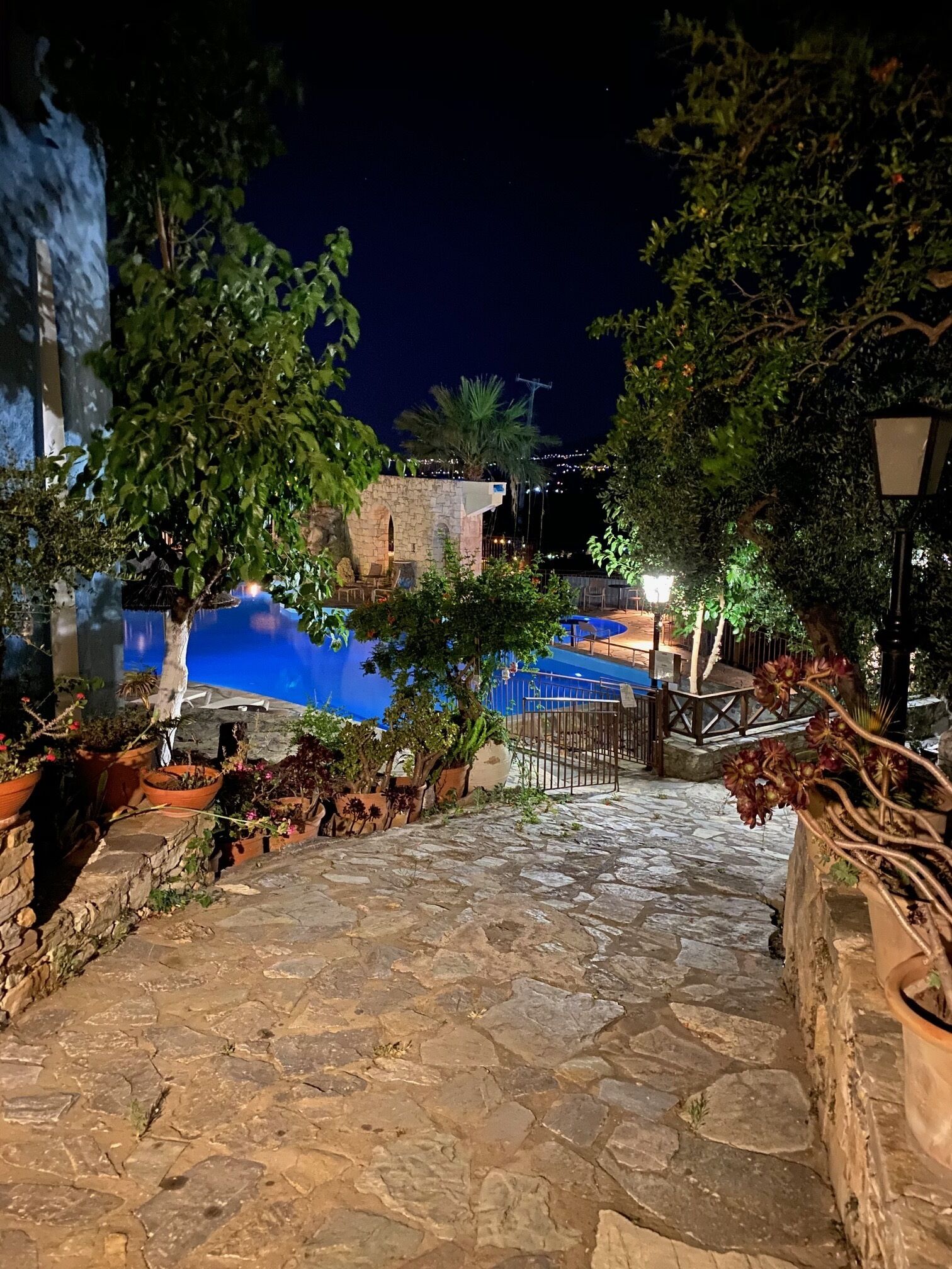 Un sendero de piedra que conduce a una zona de piscina con un edificio de piedra y plantas en macetas.