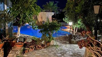 Un sendero de piedra que conduce a una zona de piscina con un edificio de piedra y plantas en macetas.