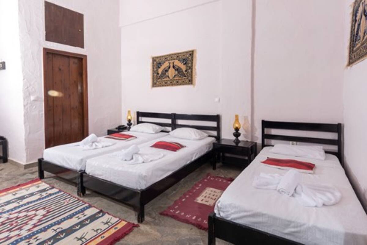 Ein Zimmer mit zwei Einzelbetten, einer Holztür, einem an der Wand hängenden Kunstwerk und einem gemusterten Teppich.