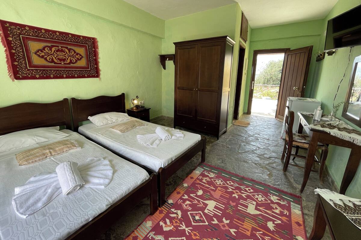 Ein Zimmer mit zwei Betten, einem Schrank, einem Schreibtisch mit Computer und einem Teppich mit Muster.
