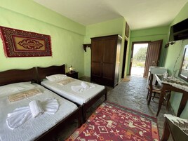 Una habitación con dos camas, un armario, un escritorio con una computadora y una alfombra estampada.
