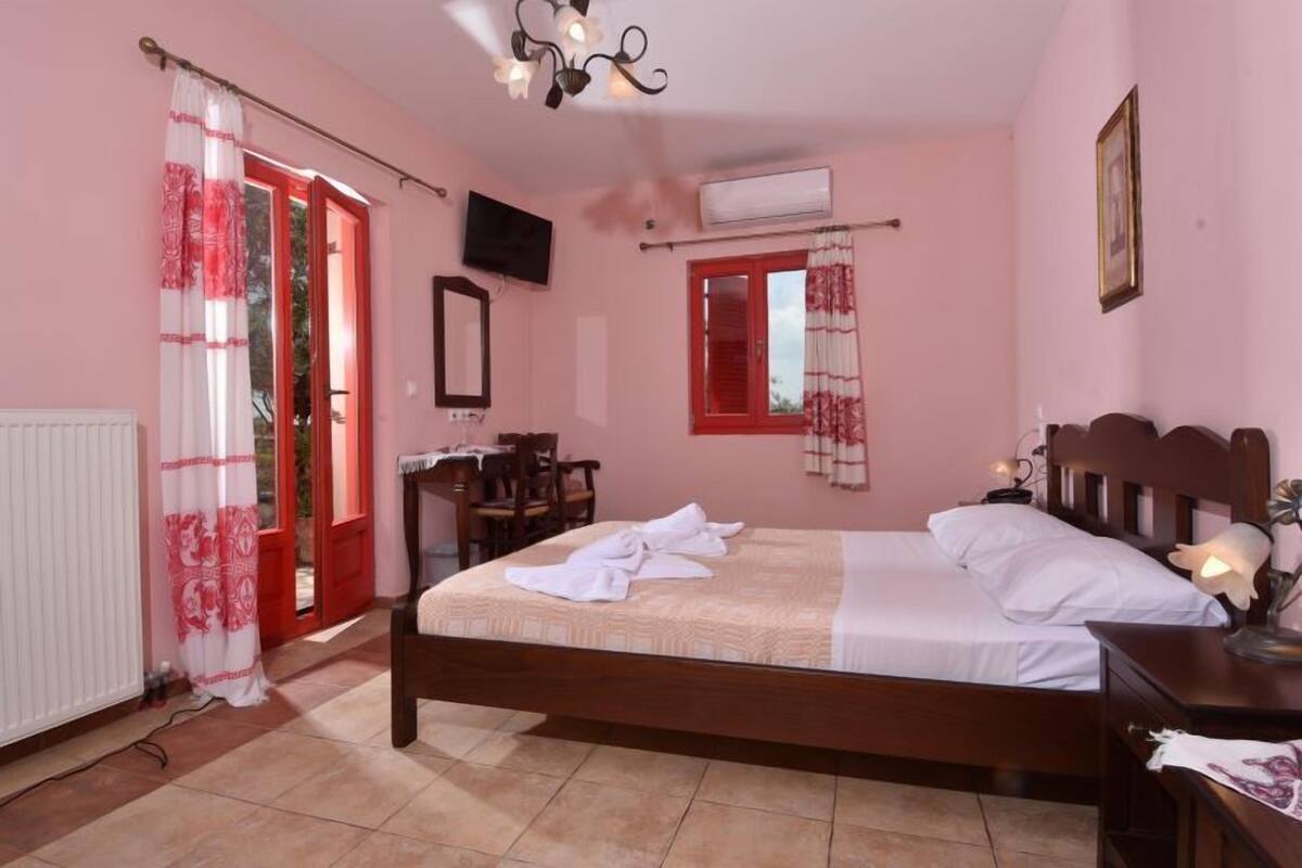 Ein Schlafzimmer mit einem Bett, einem Schreibtisch, einem Stuhl, einem Fernseher und einem Fenster mit roten Fensterläden.