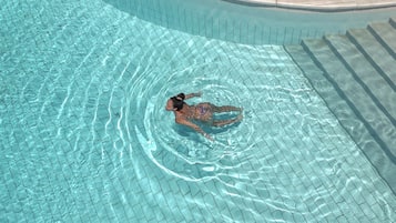 A swimming pool with clear water, a tiled edge, and a stone-tiled deck area.