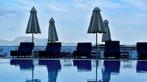 Zona junto a la piscina con sillones de descanso y sombrillas, vista despejada al mar y montañas al fondo.