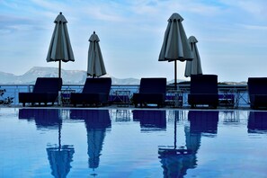Zona junto a la piscina con sillones de descanso y sombrillas, vista despejada al mar y montañas al fondo.