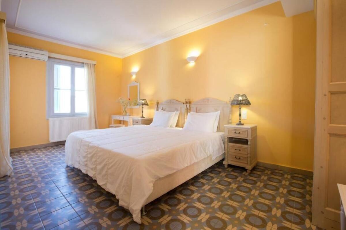 Un dormitorio con cama, mesitas de noche, una ventana y suelo con baldosas estampadas.