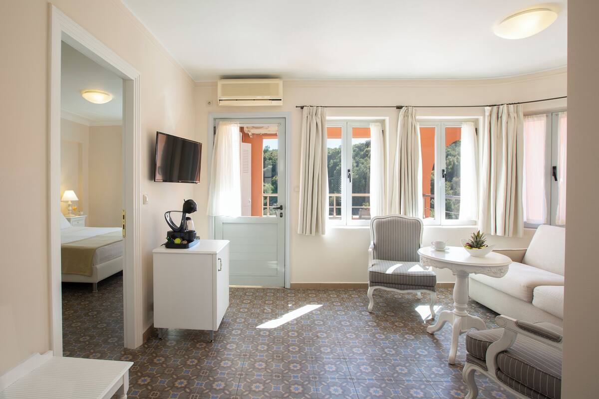 Habitación de hotel con cama, escritorio, televisor, silla, sofá y ventana con cortinas.