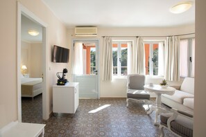 A hotel room with a bed, a desk, a TV, a chair, a sofa, and a window with curtains. - Red Tower (Lefkada)