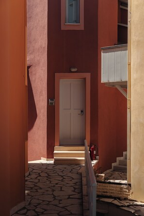 A narrow corridor with a white door, a fire extinguisher, and a small window. - Red Tower (Lefkada)