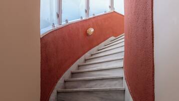 A marble staircase with a red wall on one side and a white wall on the other, leading to a room with a sloped ceiling and large windows.