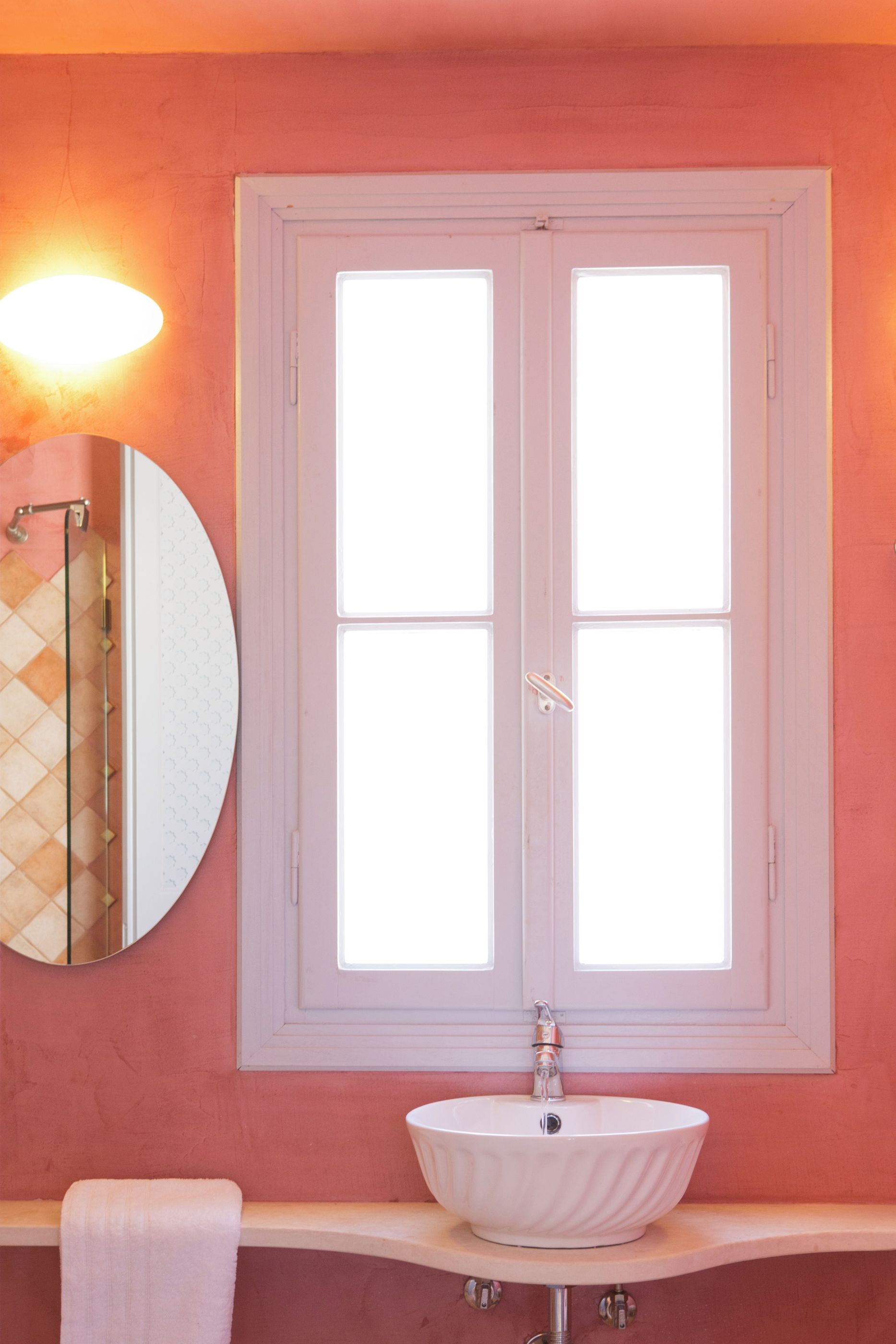 A bathroom with a white sink, a round mirror, and a window with white frames.