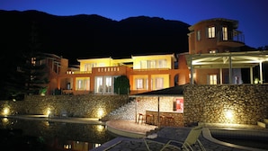Un edificio de varios pisos con piscina, paredes de piedra y mobiliario exterior.