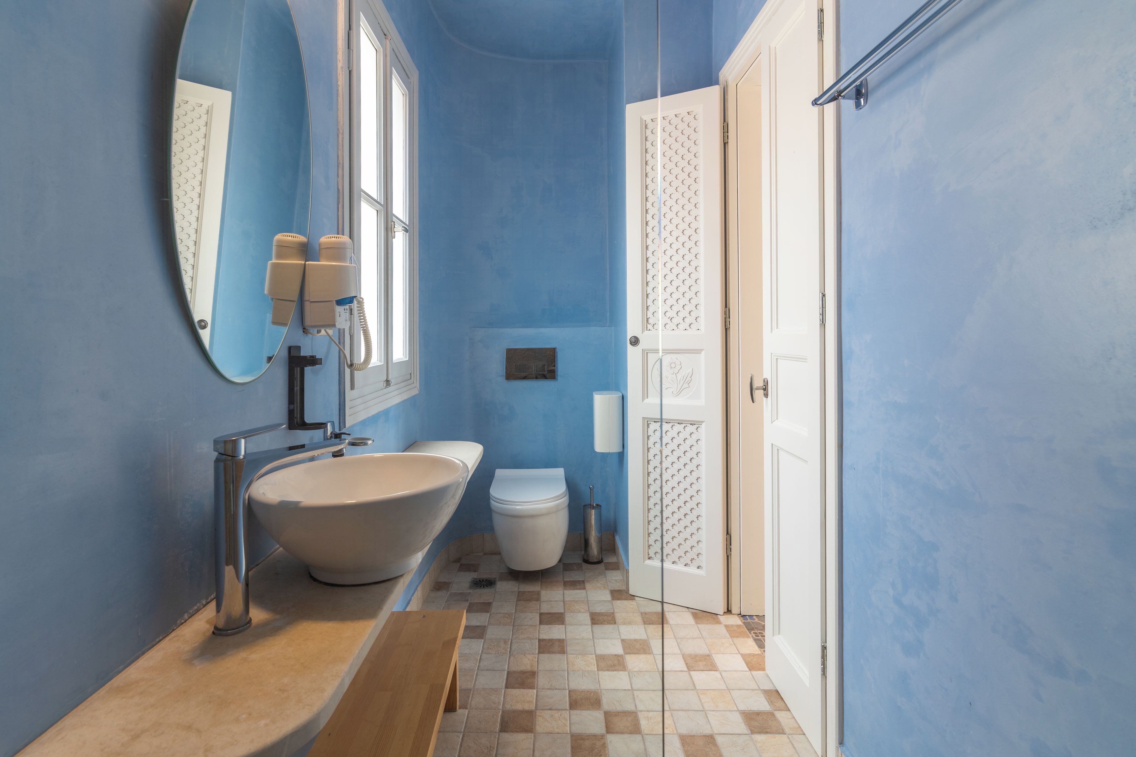 Une salle de bain avec un grand miroir ovale, un lavabo, des toilettes et une porte ornée d’un panneau décoratif.