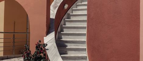 A spiral staircase leading to a building with a red exterior. There is a large potted plant at the base of the stairs.
