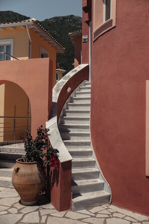 A spiral staircase leading to a building with a red exterior. There is a large potted plant at the base of the stairs. - Red Tower (Lefkada)