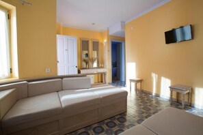 A living room with a beige sofa, a small table, and a TV mounted on the wall. - Red Tower (Lefkada)
