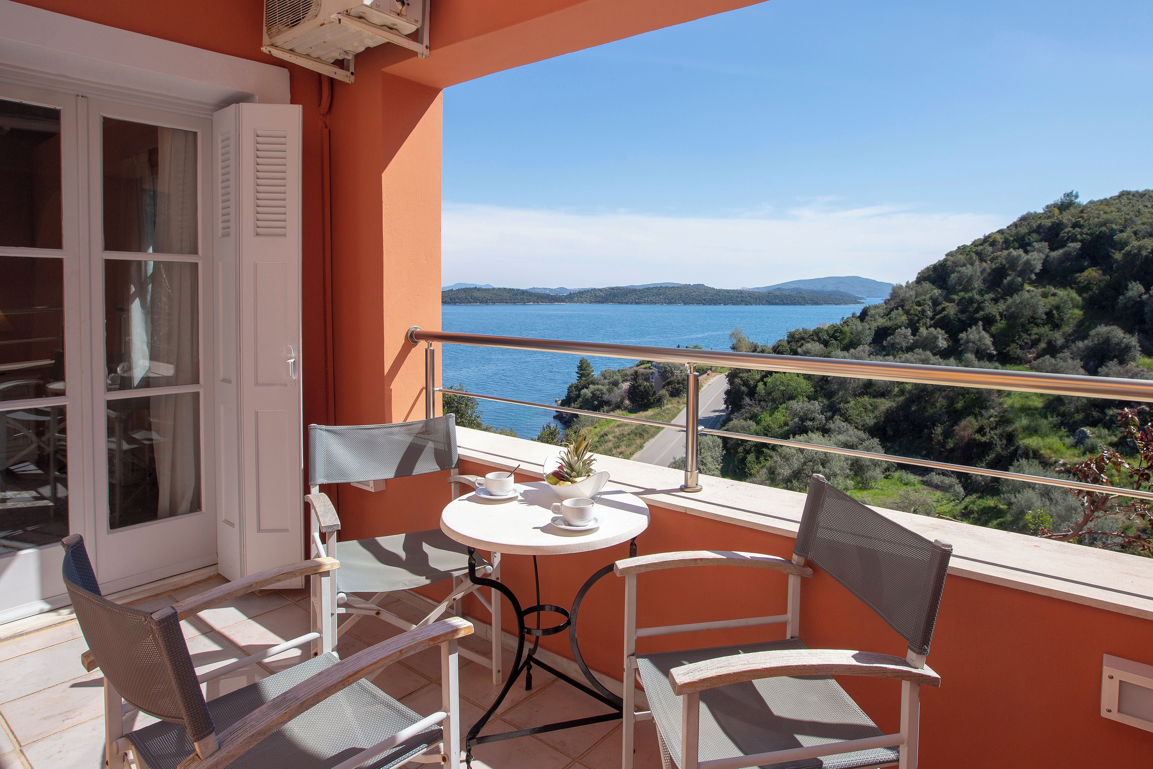 A balcony with a table and chairs, overlooking a lake and hills.