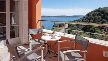 A balcony with a table and chairs, overlooking a lake and hills.