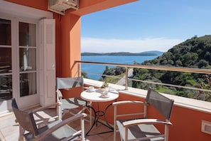 A balcony with a table and chairs, overlooking a lake and hills.