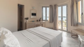 A bedroom with a large bed, a desk, a chair, and a view of the sea through a glass door. - Red Tower (Lefkada)