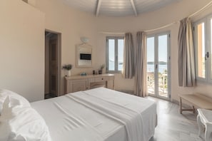 Een slaapkamer met een bed, bureau, stoel, spiegel en uitzicht op zee door een glazen deur.