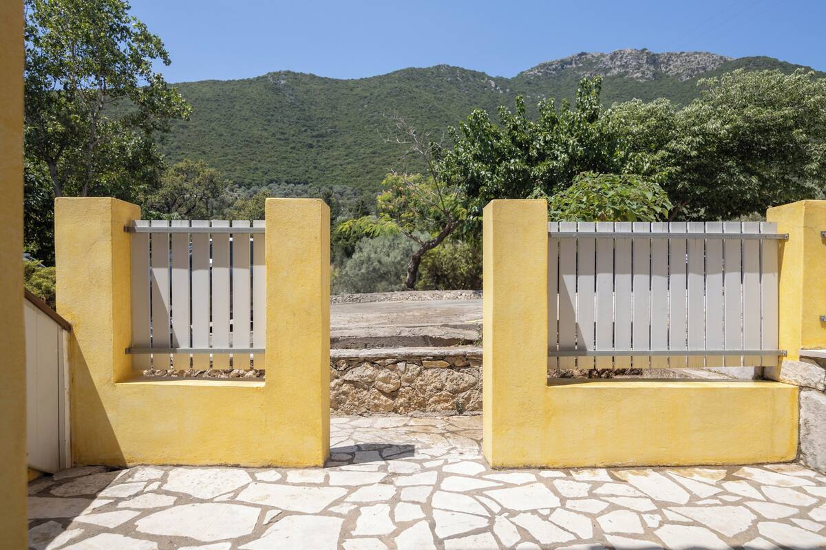 Una verja amarilla con un sendero de piedra que lleva a un paisaje montañoso.