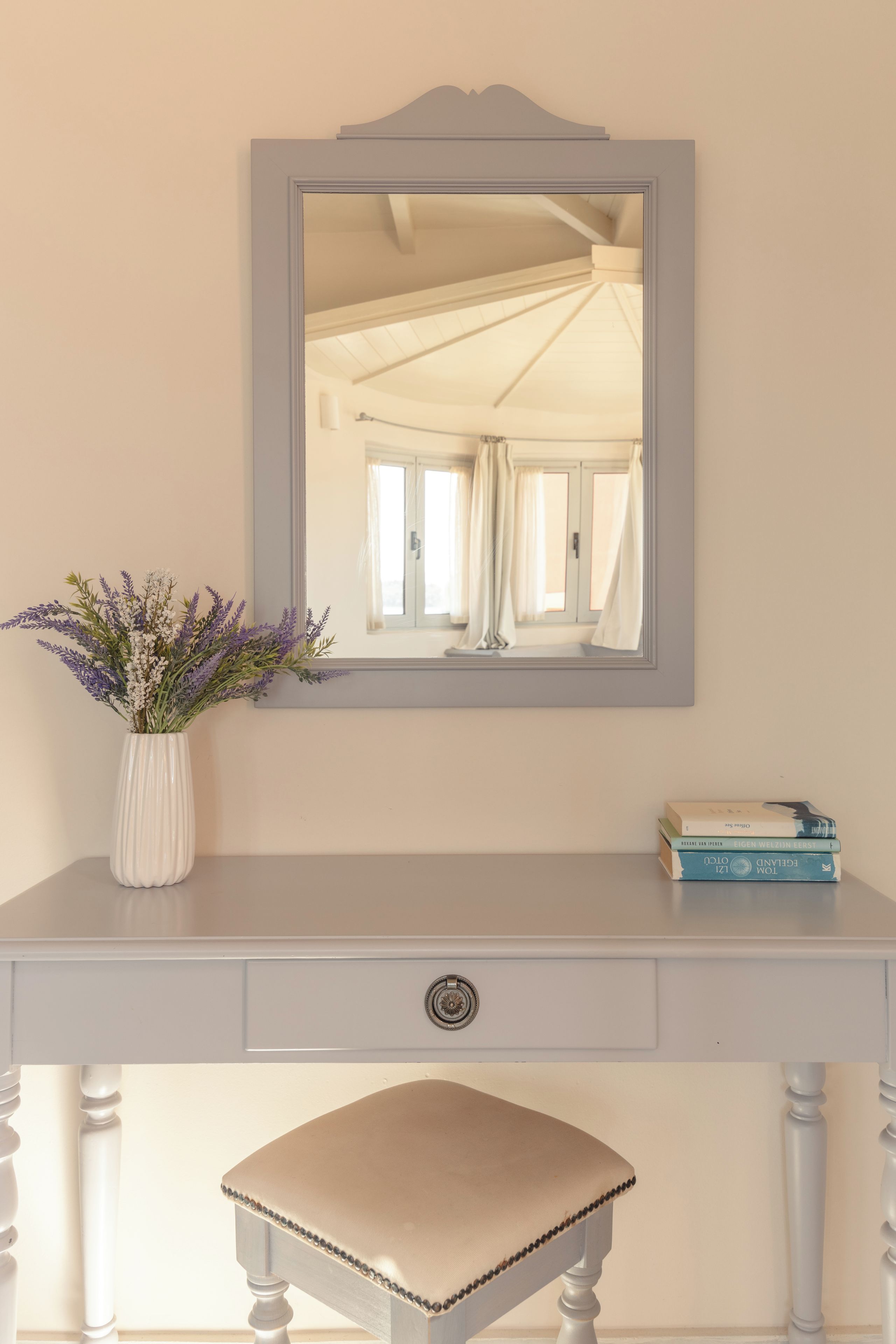 A white vanity with a mirror, a vase of flowers, and a stack of books.