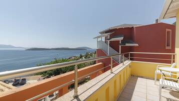 A balcony with a view of the sea, a yellow wall, and a white table and chair.