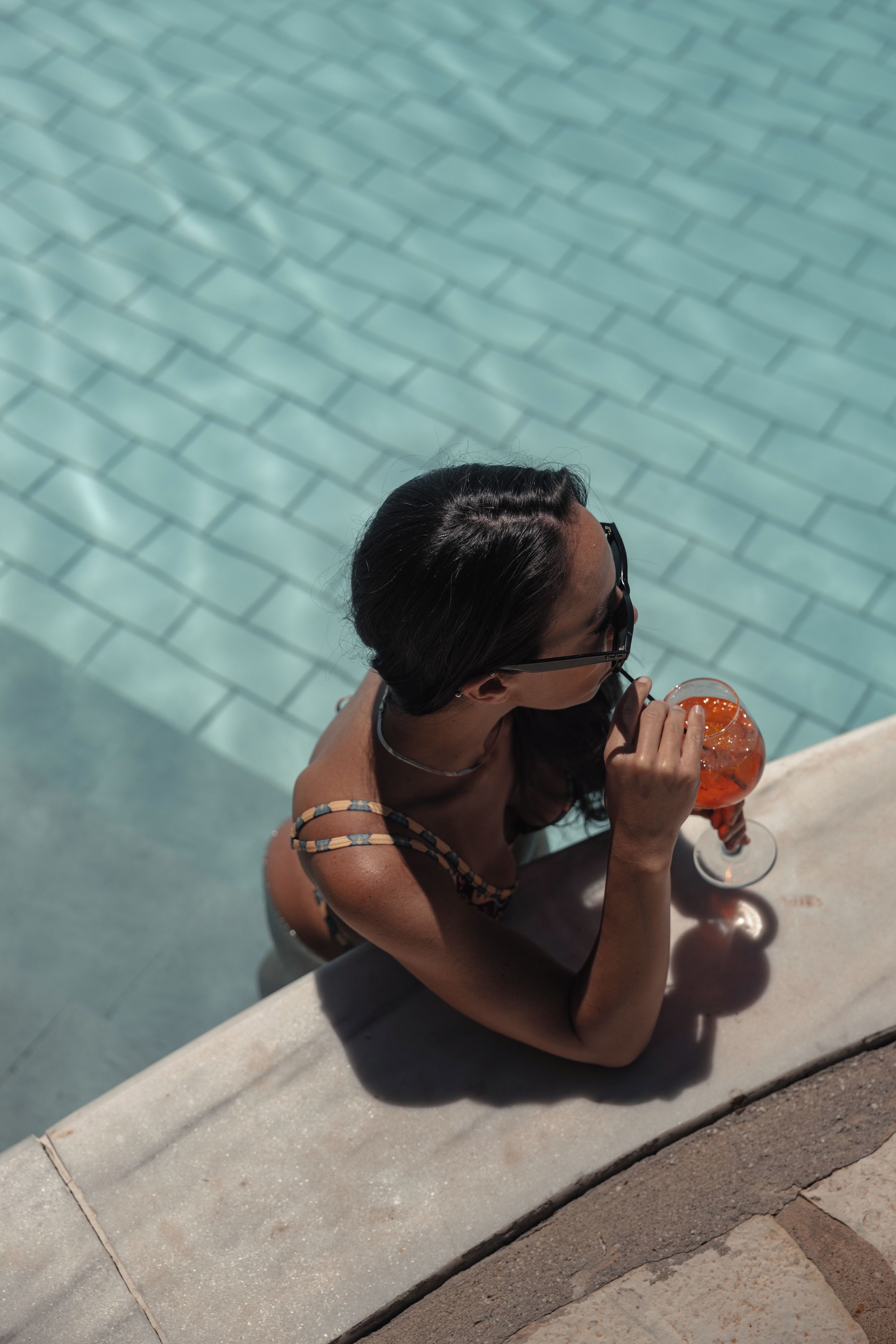 Una persona seduta a bordo piscina con un drink.