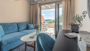 A modern living room with a blue sofa, a round table, and a view of the outdoors through a glass door. - Red Tower (Lefkada)