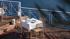 A dining area with a table set for two, overlooking a body of water and distant mountains. - Red Tower (Lefkada)