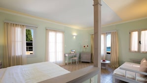 Habitación de hotel con dos camas, un escritorio, una silla, una mesita con un florero y vista al mar.